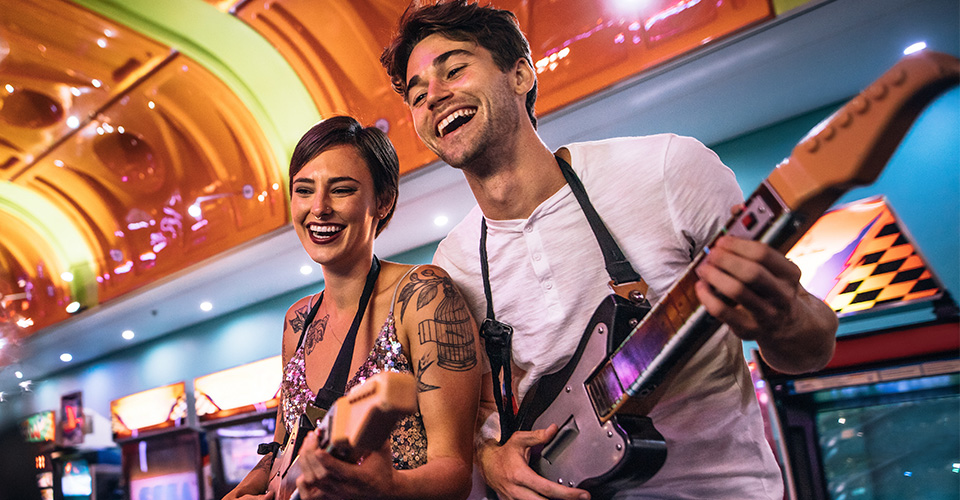 Island Social smiling man and woman playing the guitar game at a gaming arcade
